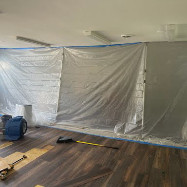 Plastic containment sheeting sealed across a room with an air mover running during mold remediation